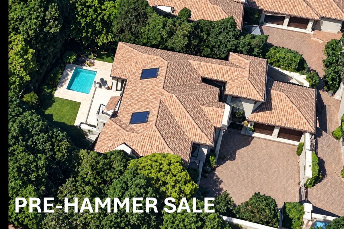Aerial view of a residential property featuring a tiled roof, skylights, a swimming pool, and a paved driveway surrounded by mature trees.