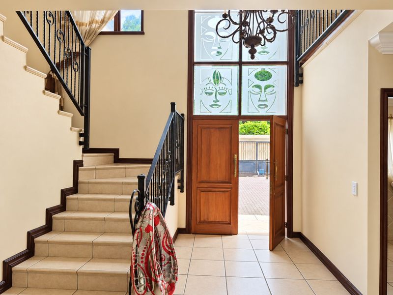 Spacious entrance hall featuring a tiled staircase with wrought iron balustrades, a double wooden front door, and decorative glass transom windows.