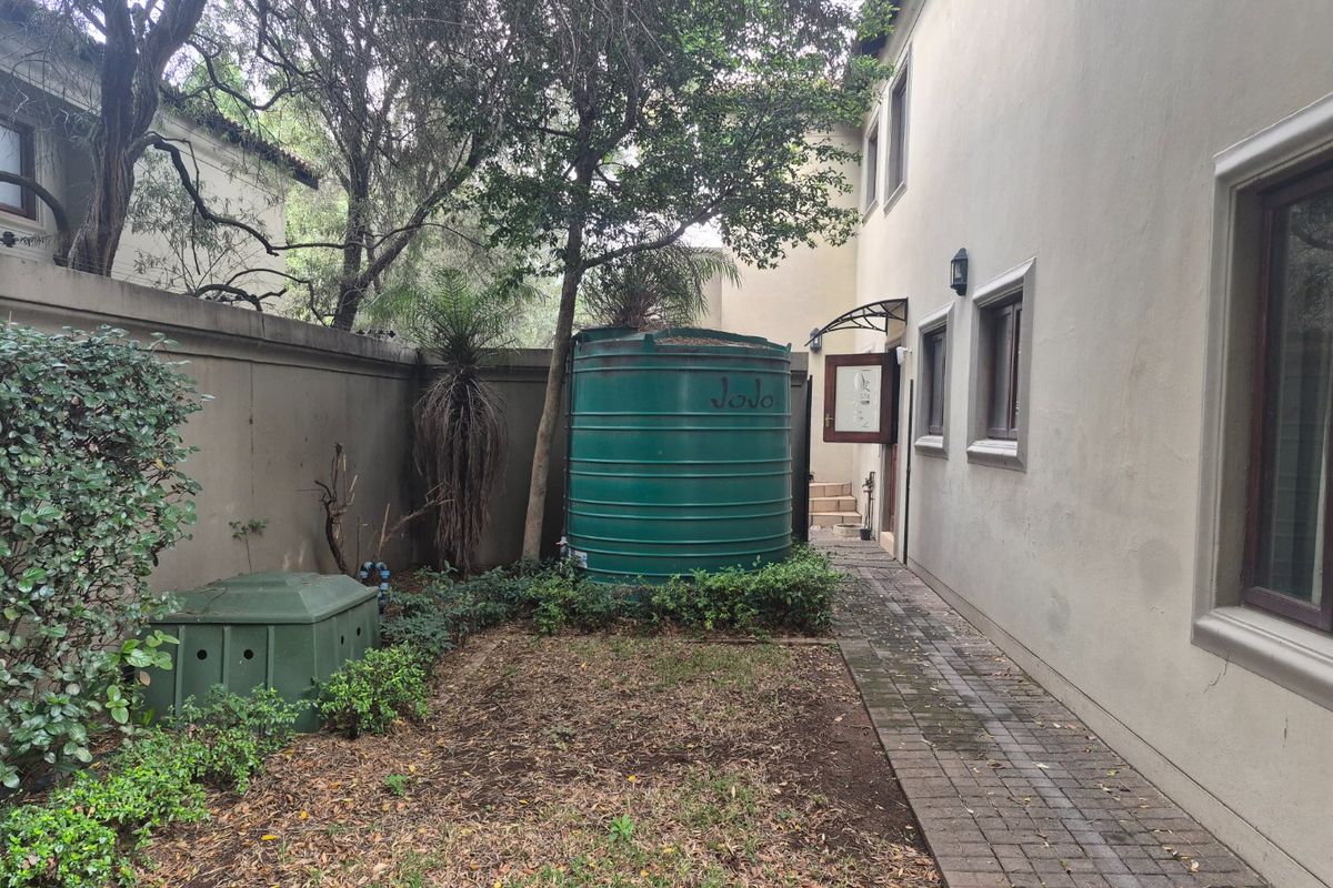 Rear exterior area featuring a paved walkway, boundary wall, and a large water storage tank adjacent to the building structure.