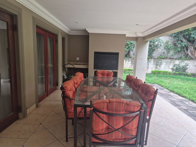 A covered patio area featuring tiled flooring, recessed lighting, and a built-in braai, providing a functional outdoor entertainment space overlooking the garden.