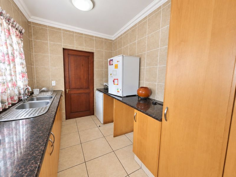 A functional scullery featuring granite countertops, double bowl stainless steel sink, and ample built-in wooden cabinetry with tiled finishes.