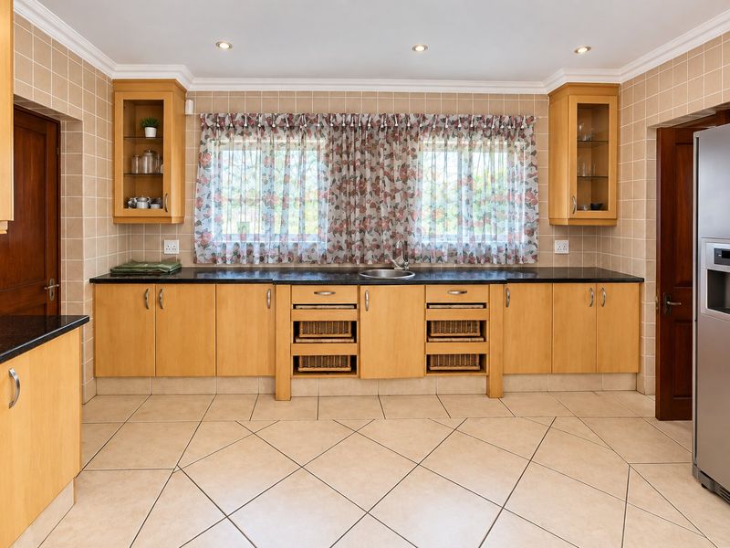 A well-maintained kitchen featuring light wood cabinetry, dark granite countertops, tiled backsplash, and neutral floor tiles with integrated storage solutions.