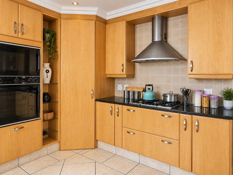 A well-maintained kitchen featuring light wood cabinetry, granite countertops, a built-in oven, and a stainless steel extractor fan with tiled flooring.