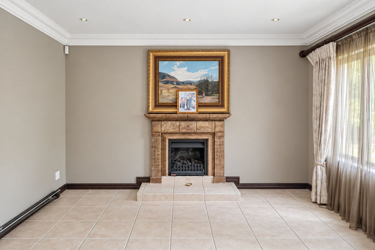A bright and spacious living room featuring a central fireplace with a tiled hearth, neutral wall tones, and large windows with elegant drapery.