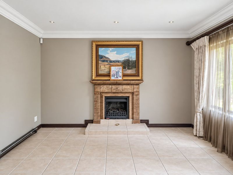 A bright and spacious living room featuring a central fireplace with a tiled hearth, neutral wall tones, and large windows with elegant drapery.