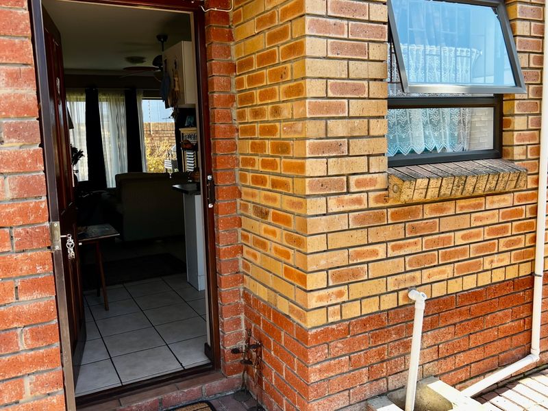 Exterior view of the apartment entrance featuring face brick facade, a top-hung window, and tiled flooring leading into the living area.