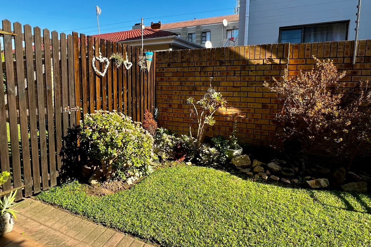 A private rear garden area featuring a well-maintained lawn, paved walkway, and a combination of brick and timber boundary fencing.