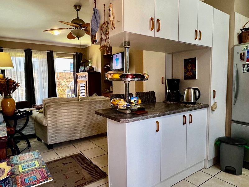 Open plan living area featuring tiled flooring, a functional kitchen with white cabinetry, and a breakfast bar connecting to the lounge space.