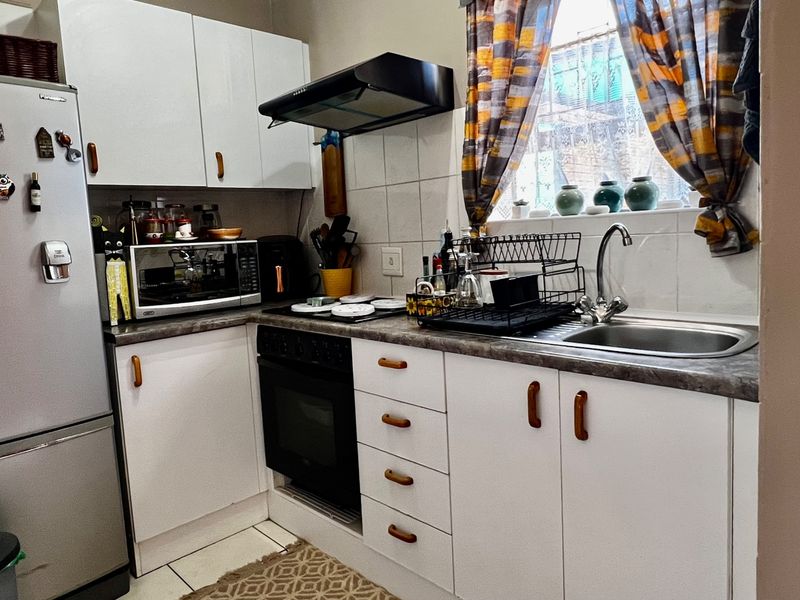 Compact kitchen featuring white cabinetry, laminate countertops, a built-in oven with extractor fan, and a stainless steel sink with tiled backsplash.