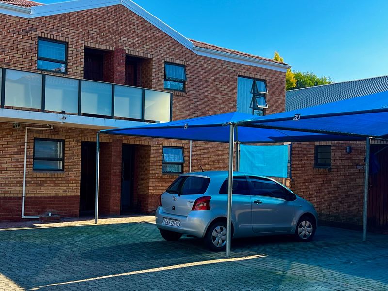Exterior view of a face brick apartment building featuring a paved driveway and a dedicated shade cloth carport for parking.