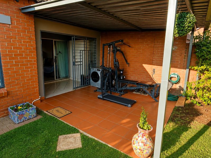 A covered outdoor patio area featuring tiled flooring, brick walls, and direct access to the interior through a sliding door with security gate.
