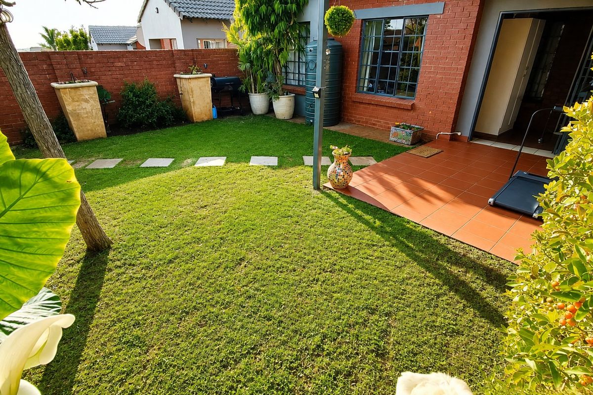 A well-maintained rear garden featuring a tiled patio area, lush lawn, and brick boundary walls, providing a private outdoor space.