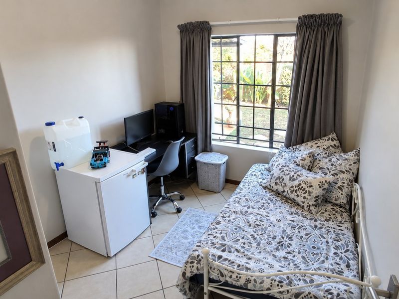 A compact bedroom featuring tiled flooring and a window with security bars, providing natural light and a view of the garden area.