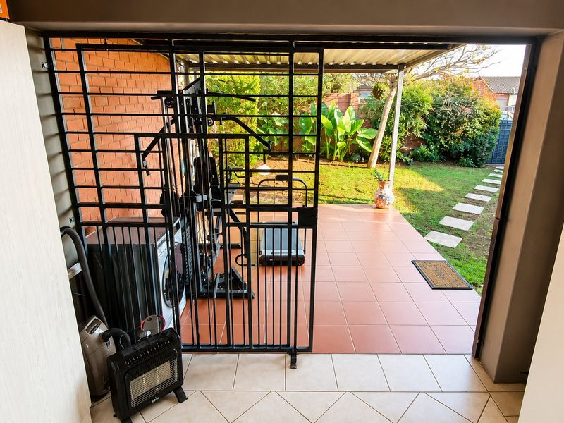 A covered patio area featuring tiled flooring, a security gate, and direct access to a landscaped garden with stone pathway.