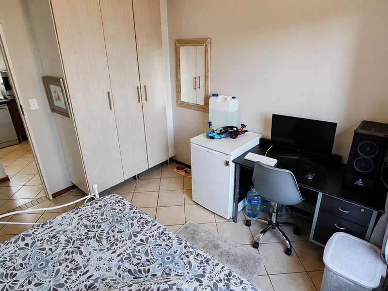 A functional bedroom featuring tiled flooring and a built-in wardrobe, with an adjacent view into a kitchen area.