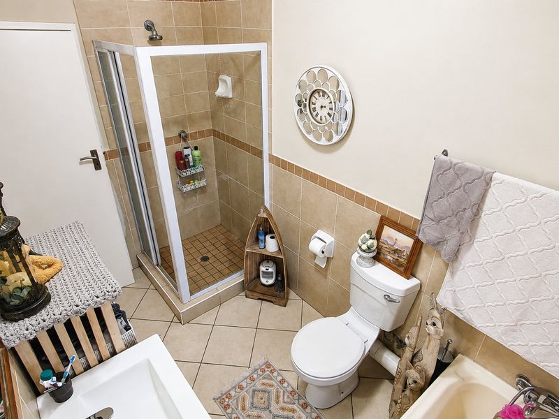 A functional bathroom featuring a shower enclosure, toilet, bathtub, and vanity basin with neutral wall and floor tiling.