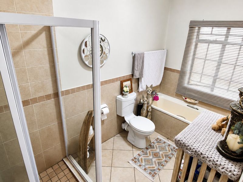 A functional bathroom featuring a separate shower enclosure, bathtub, toilet, and neutral wall and floor tiling with natural light from a window.