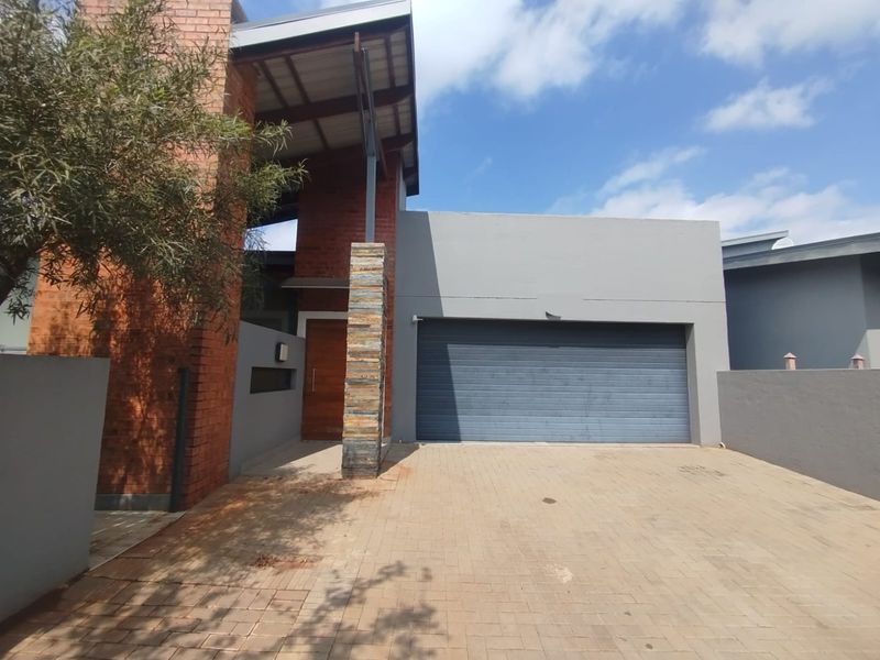 Modern front elevation featuring a combination of face brick and rendered walls, a stone-clad pillar, timber entrance door, and a paved driveway with garage.