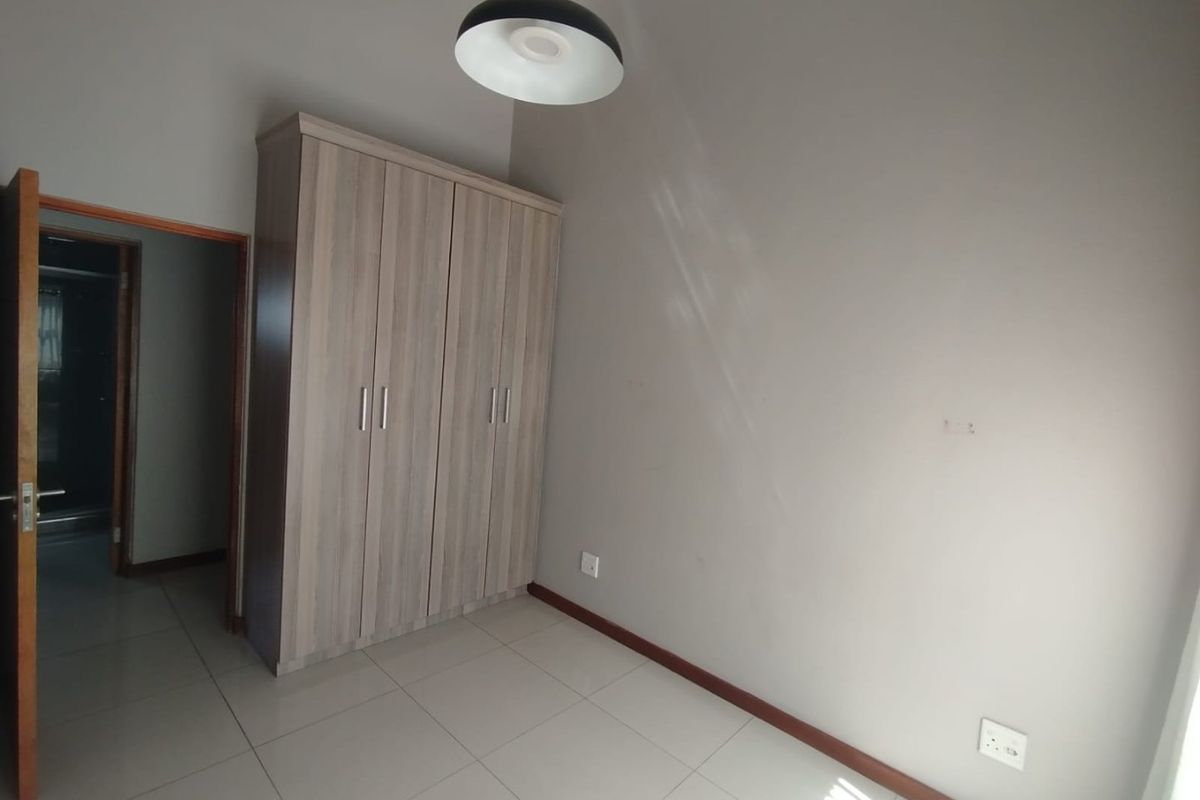 A clean, empty bedroom featuring neutral tiled flooring, a modern built-in wardrobe, and a contemporary pendant light fixture.