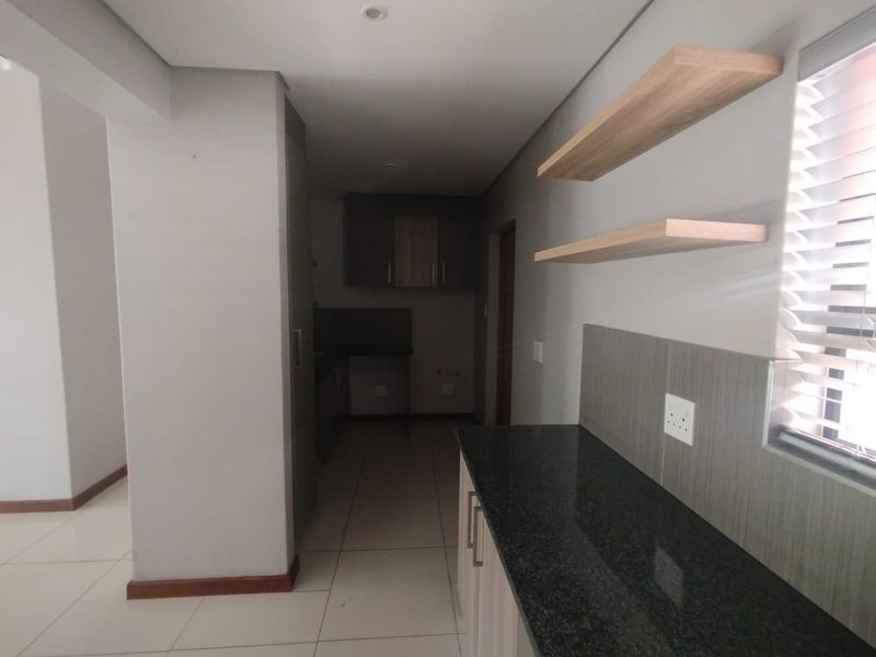 A modern, empty kitchen featuring granite countertops, built-in cabinetry, floating shelves, and neutral tiled flooring with clean finishes.
