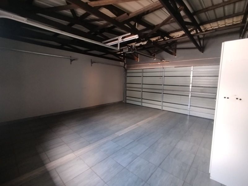 A clean, spacious double garage featuring tiled flooring, exposed roof trusses, and an automated sectional garage door.