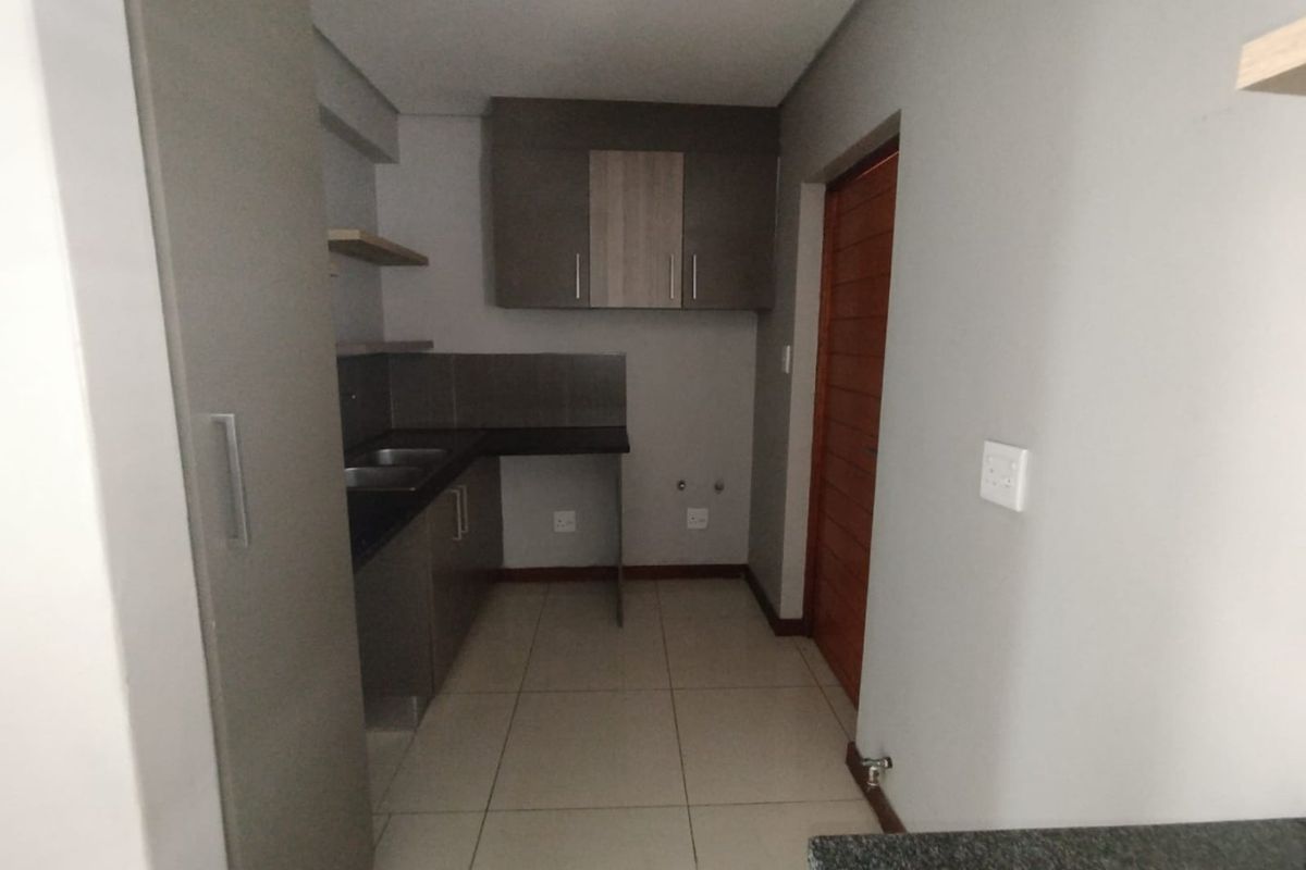 A clean, modern kitchen featuring neutral cabinetry, dark countertops, tiled flooring, and dedicated plumbing connections for appliances.