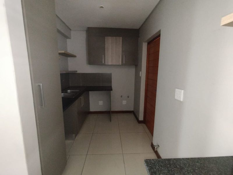 A clean, modern kitchen featuring neutral cabinetry, dark countertops, tiled flooring, and dedicated plumbing connections for appliances.