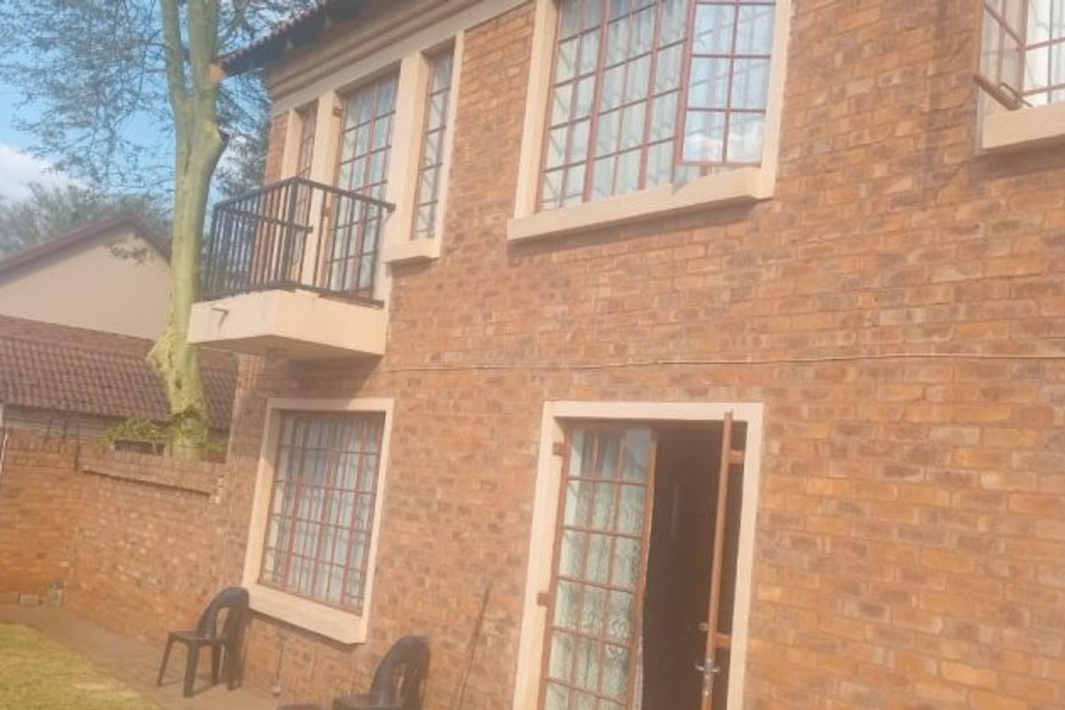 Rear view of a double-story face brick house featuring a small balcony with metal railing and secure steel-framed windows.