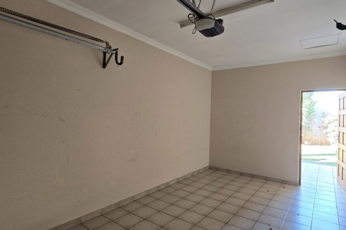 A spacious, empty garage featuring tiled flooring, a garage door motor, and a rear access door leading to the garden area.