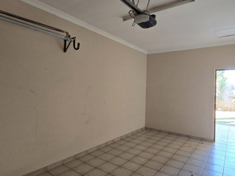 A spacious, empty garage featuring tiled flooring, a garage door motor, and a rear access door leading to the garden area.