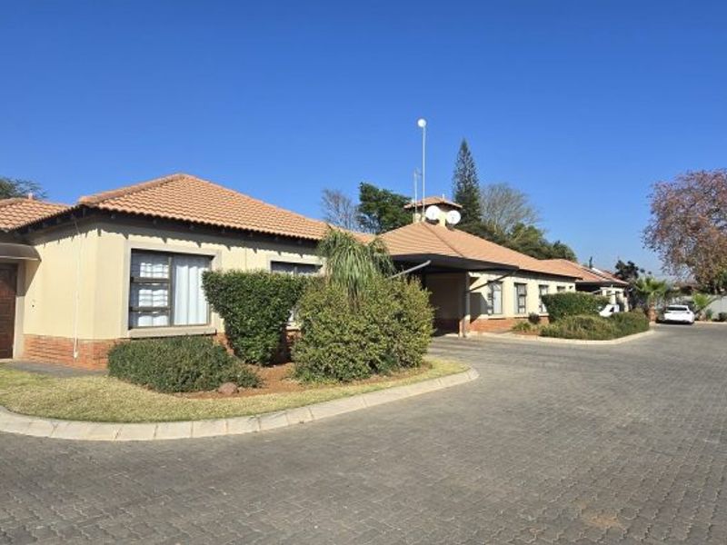 Front exterior view of a townhouse complex featuring a paved driveway, tiled roof, and established garden landscaping.