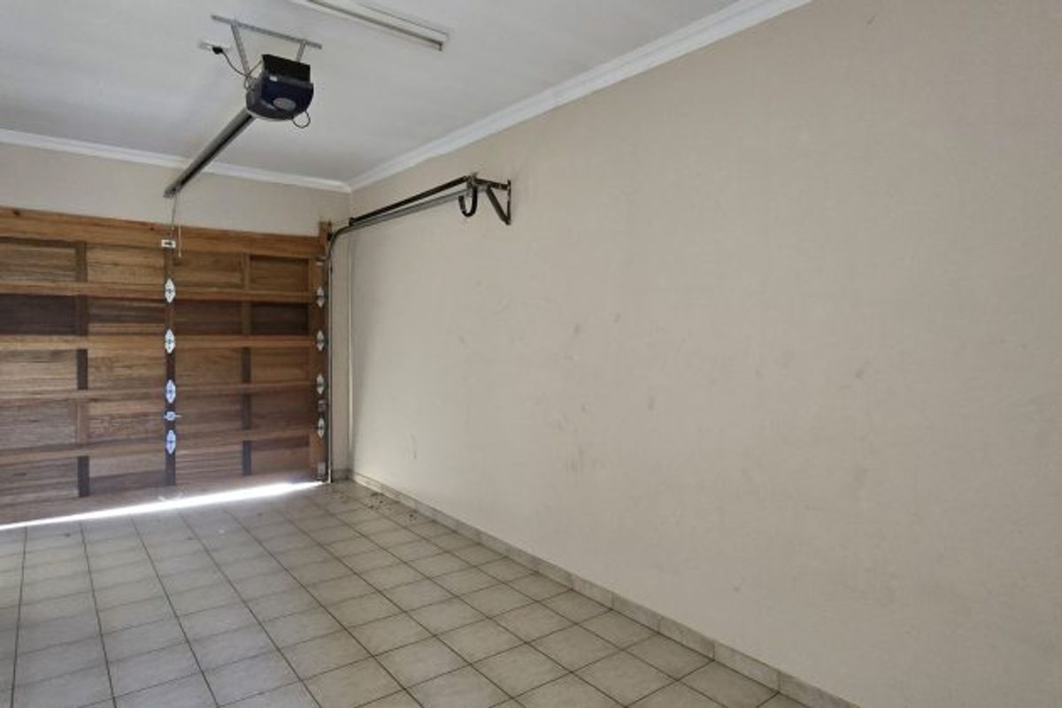 A spacious, empty garage featuring a sectional wooden door, automatic opener, and tiled flooring, providing secure parking or additional storage space.