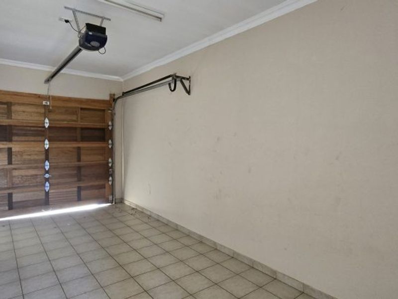 A spacious, empty garage featuring a sectional wooden door, automatic opener, and tiled flooring, providing secure parking or additional storage space.