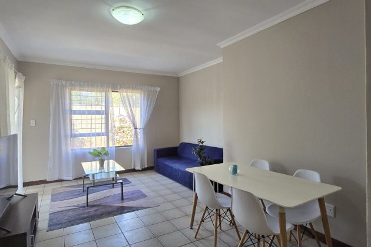 An open-plan living and dining area featuring tiled flooring, neutral wall tones, and a window fitted with security bars.