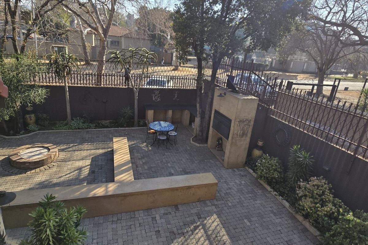 A paved rear courtyard featuring a built-in braai, a circular brick fire pit, and integrated concrete seating, enclosed by perimeter fencing.