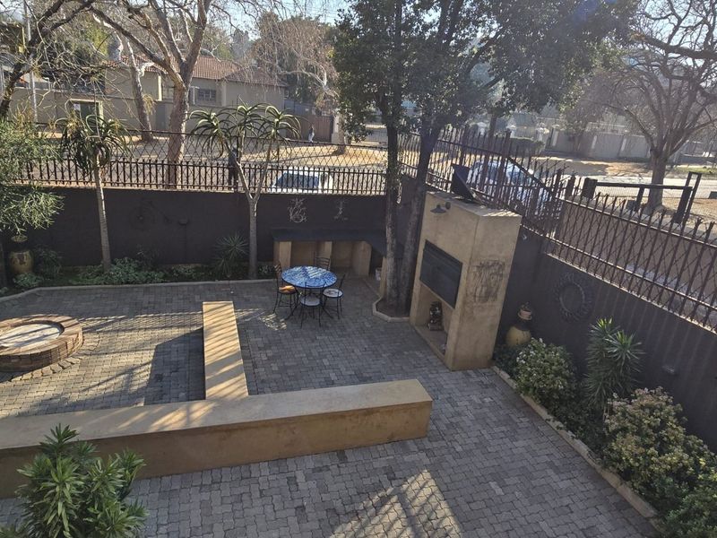 A paved rear courtyard featuring a built-in braai, a circular brick fire pit, and integrated concrete seating, enclosed by perimeter fencing.