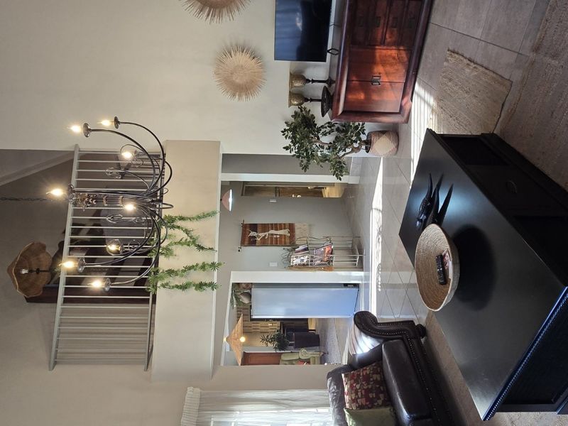 Spacious living area featuring a high vaulted ceiling with exposed beams, a mezzanine level with a metal balustrade, and tiled flooring.