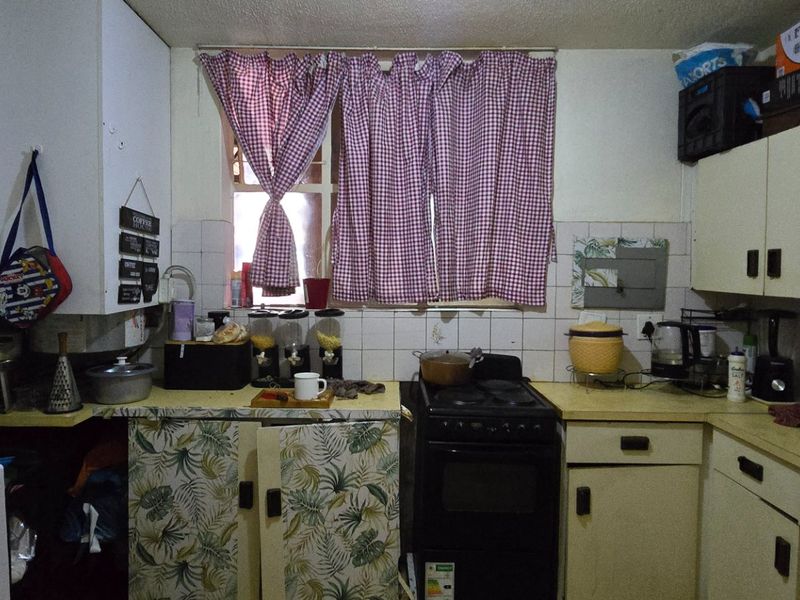 A functional kitchen featuring built-in cabinetry, laminate countertops, a tiled backsplash, and a freestanding stove, offering potential for modernization and cosmetic updates.