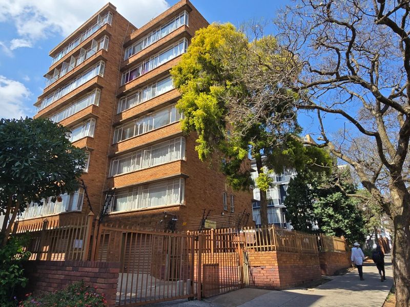 A multi-story brick apartment building featuring secure perimeter fencing and electric security measures, situated along a street-front.