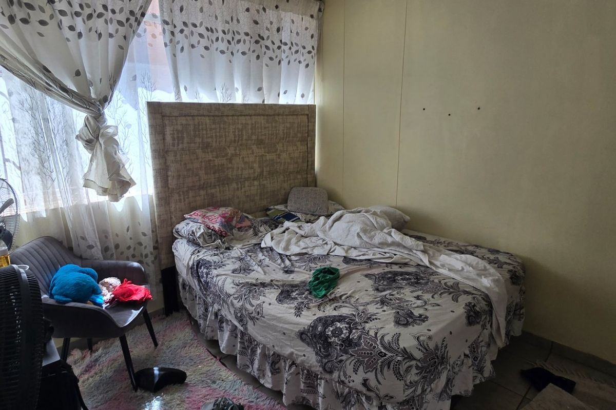 A bedroom featuring tiled flooring and a large window, currently requiring cosmetic updates to the wall finishes.