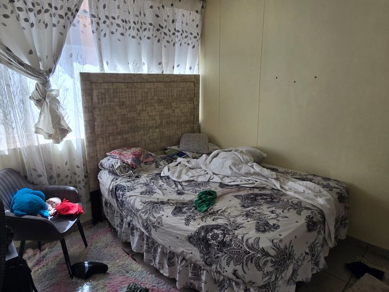 A bedroom featuring tiled flooring and a large window, currently requiring cosmetic updates to the wall finishes.
