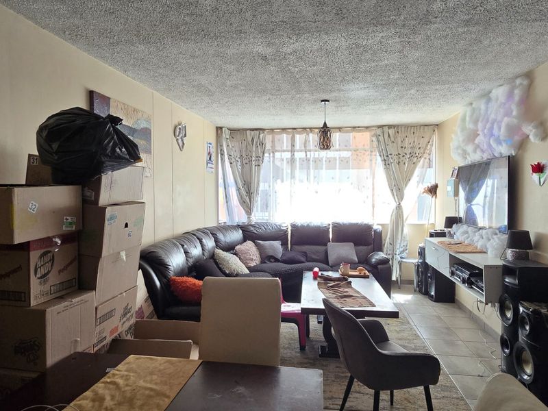 A living room area featuring tiled flooring and a large window, providing natural light. The space requires cosmetic updates to improve its overall appeal.