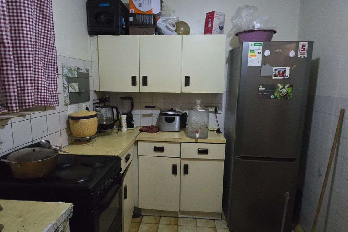 A compact kitchen featuring dated cabinetry, tiled backsplash, and tiled flooring, offering potential for a modern renovation to enhance functionality and aesthetic appeal.