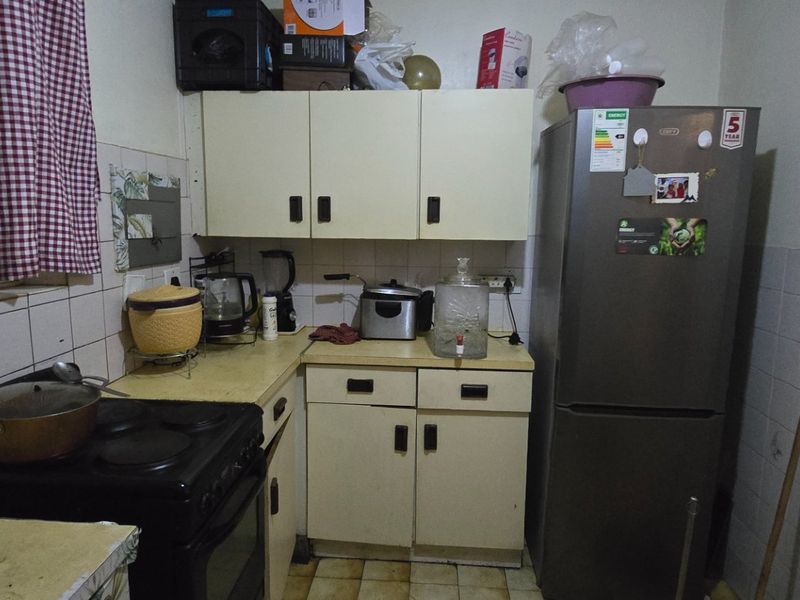 A compact kitchen featuring dated cabinetry, tiled backsplash, and tiled flooring, offering potential for a modern renovation to enhance functionality and aesthetic appeal.