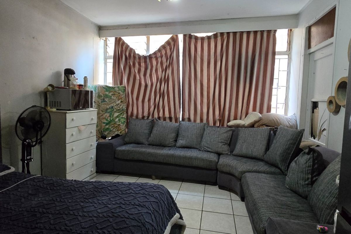 A living area featuring tiled flooring and large windows with security bars, currently showing signs of wear and requiring cosmetic updates.