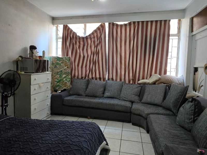 A living area featuring tiled flooring and large windows with security bars, currently showing signs of wear and requiring cosmetic updates.