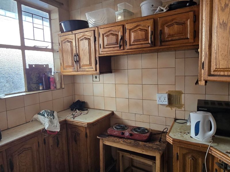 A dated kitchen featuring traditional wooden cabinetry, tiled backsplash, and a large window, requiring modernization of finishes and fixtures.