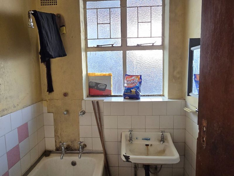 A dated bathroom featuring a bathtub, pedestal sink, and steel-framed window, requiring significant renovation and cosmetic updates to improve its condition.