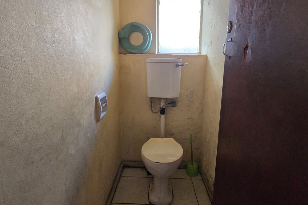 A small, dated bathroom featuring a standard toilet and tiled flooring, currently in need of significant cosmetic renovation and wall repairs.