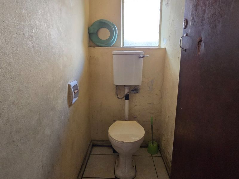 A small, dated bathroom featuring a standard toilet and tiled flooring, currently in need of significant cosmetic renovation and wall repairs.